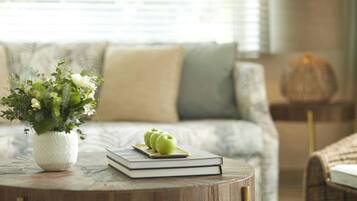 Una mesa redonda de madera con un jarrón blanco lleno de flores, un libro y dos manzanas verdes.