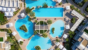 An aerial view of a resort with multiple swimming pools, sun loungers, and palm trees.