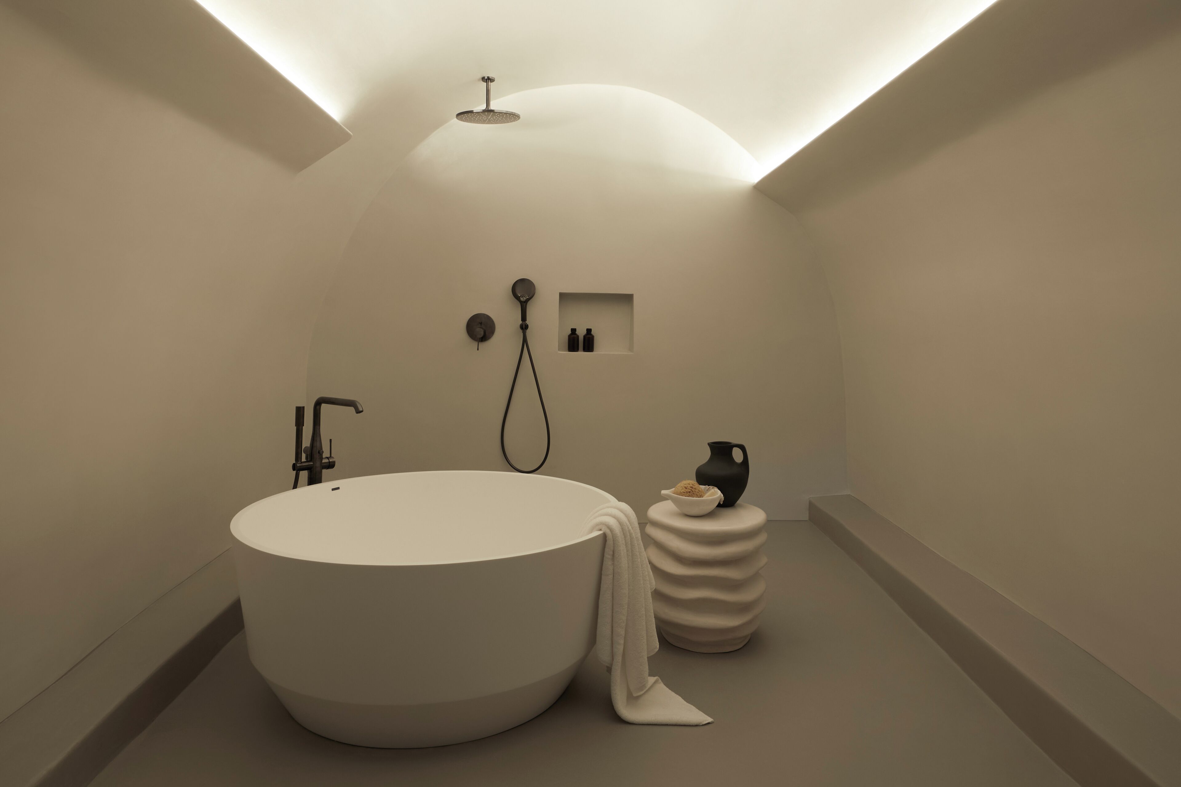 Un baño moderno con una bañera grande, un cabezal de ducha y un estante pequeño con artículos de aseo.