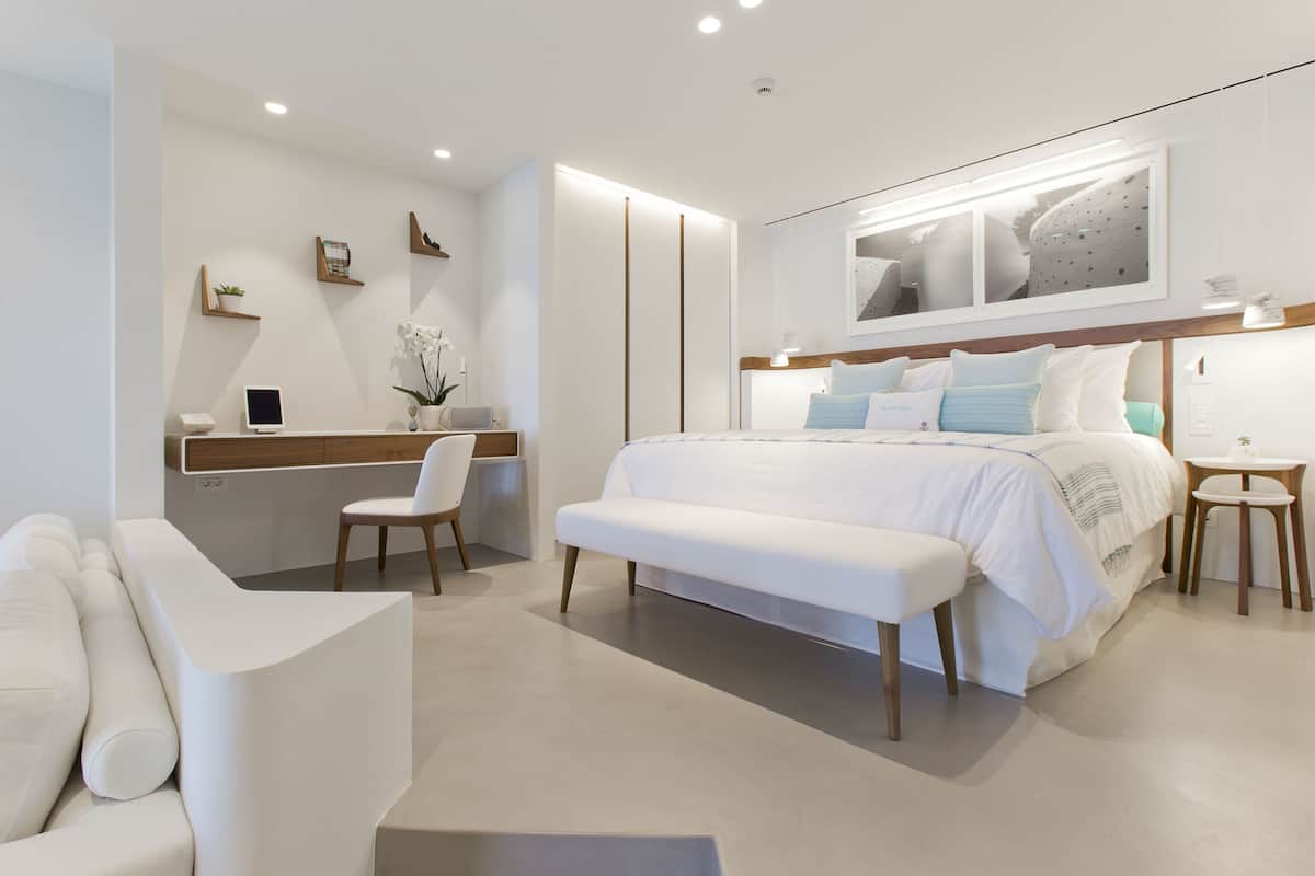A modern bedroom with a large bed, a bedside table, a chair, and a desk with a computer.