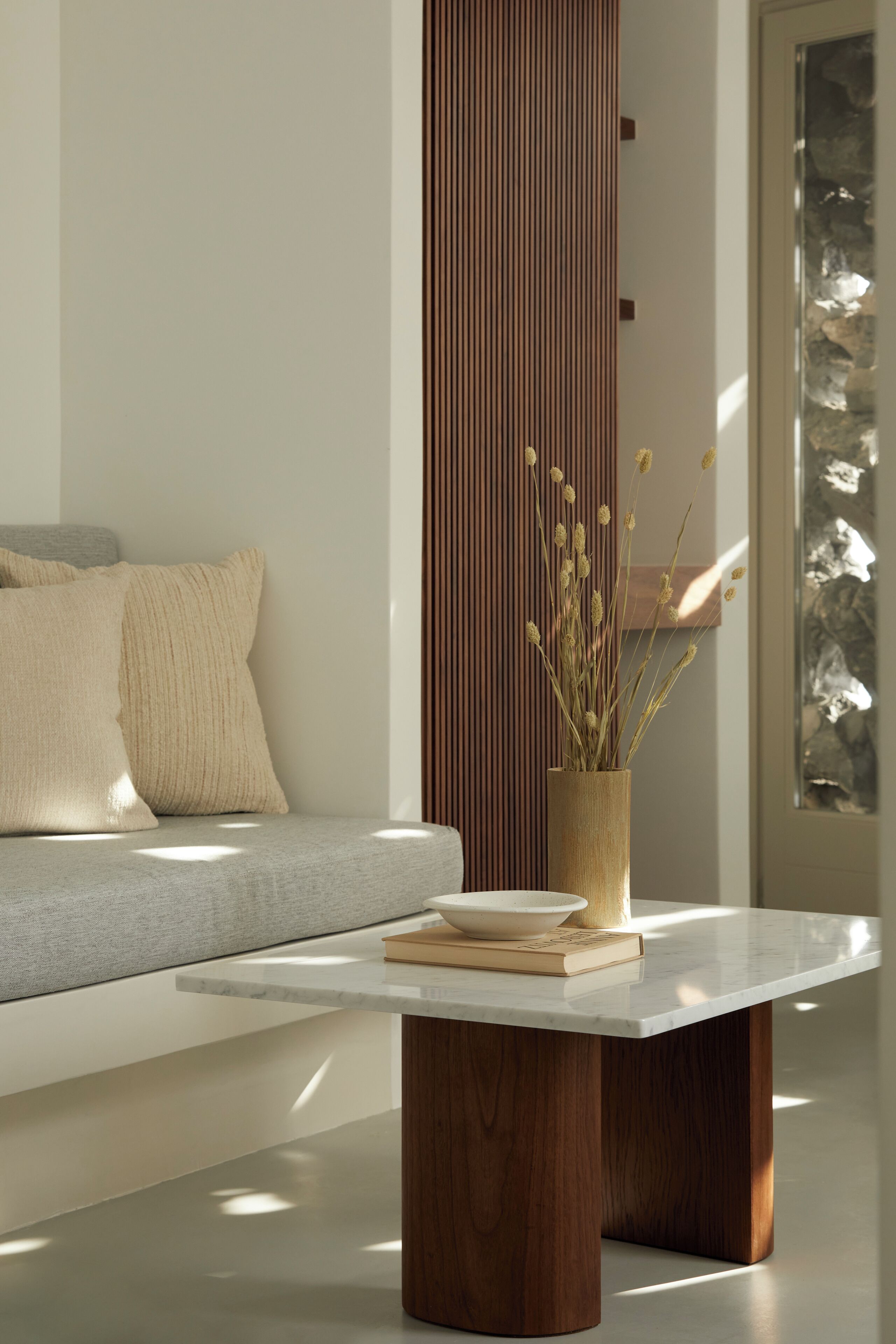 A modern living room with a sofa, a wooden sideboard, a marble coffee table, and a vase with dried plants.