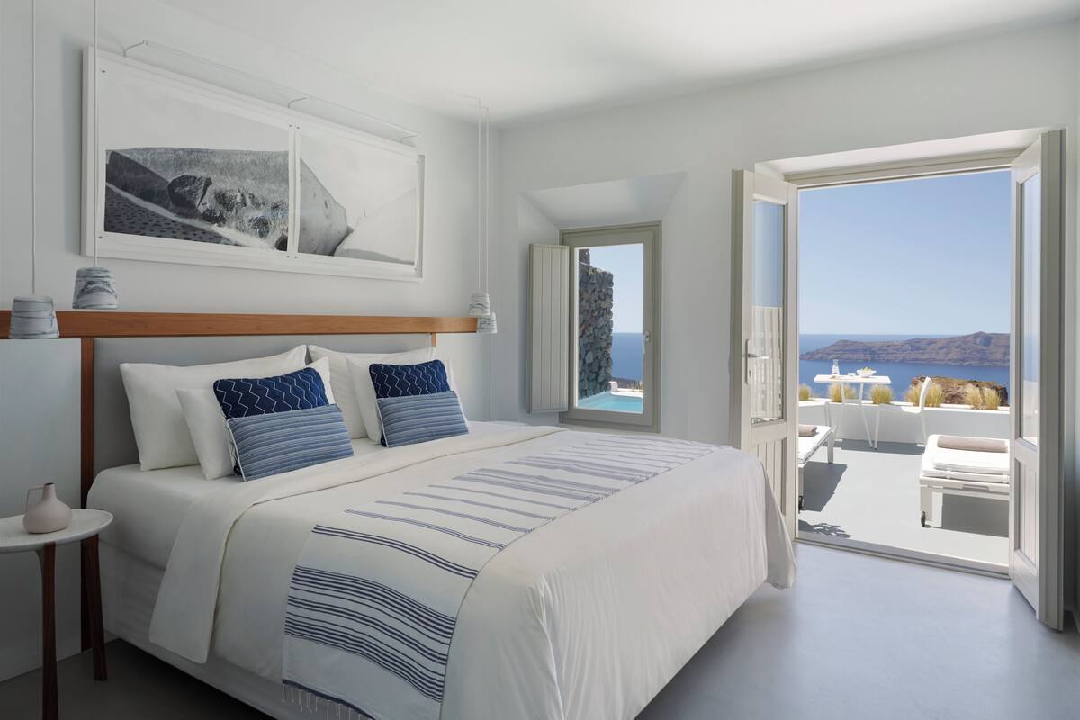 A bedroom with a large bed, a view of the sea, and a balcony with outdoor furniture.
