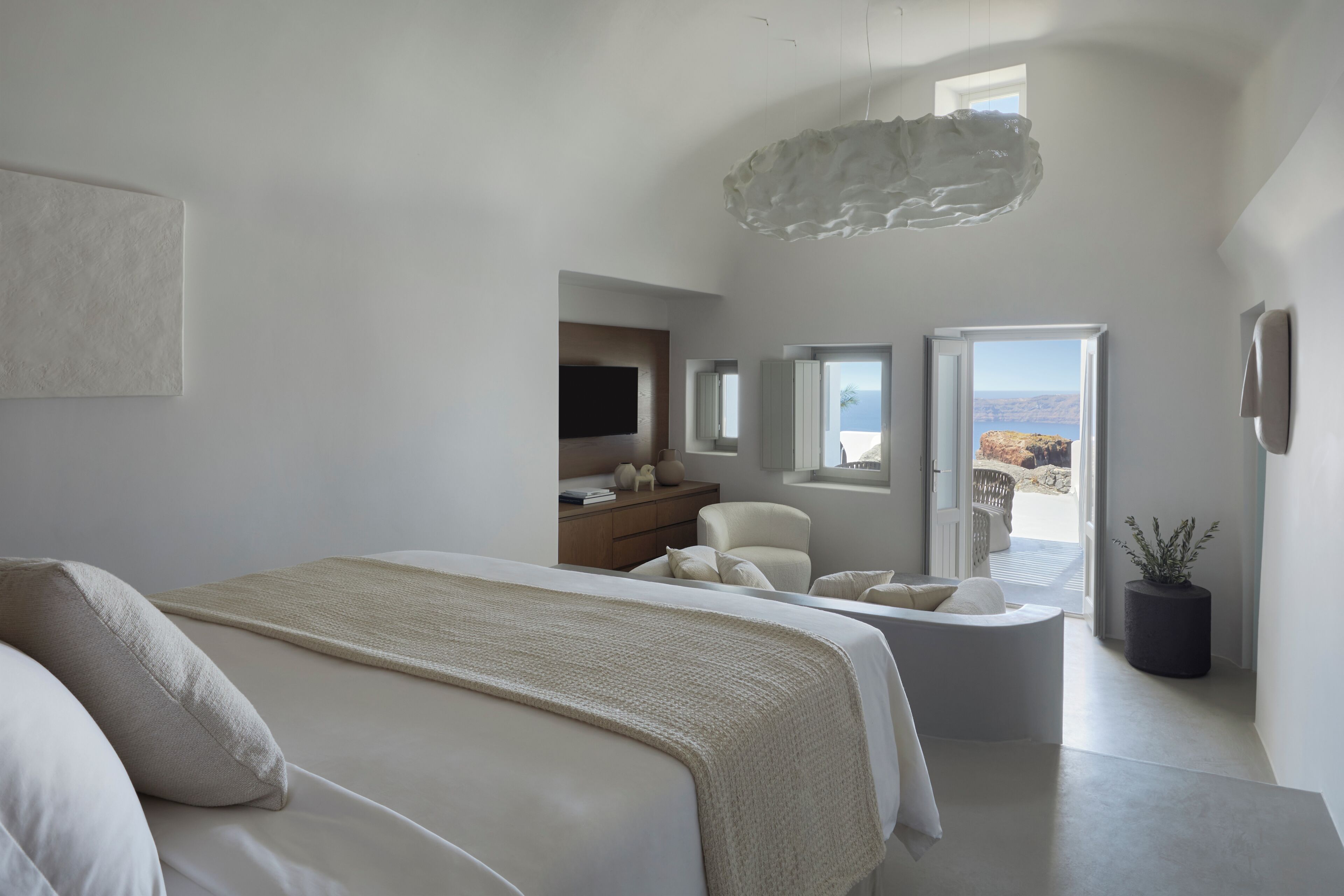 A modern bedroom with a large bed, a seating area, a television, and a view of the outdoors.