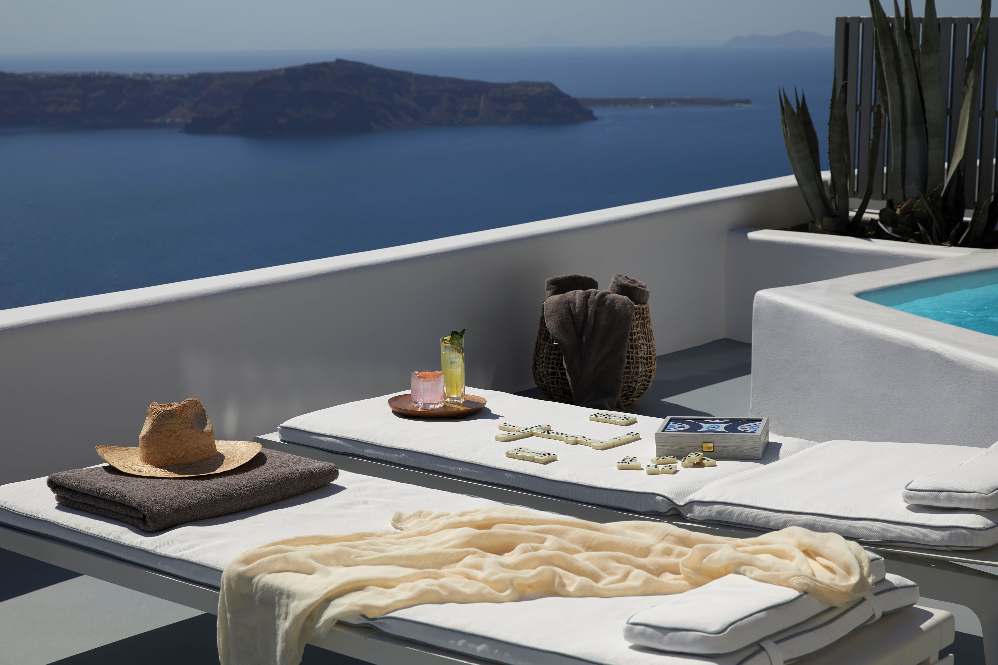 Un balcon ensoleillé avec vue sur la mer, une piscine et des chaises longues avec des serviettes et un chapeau.