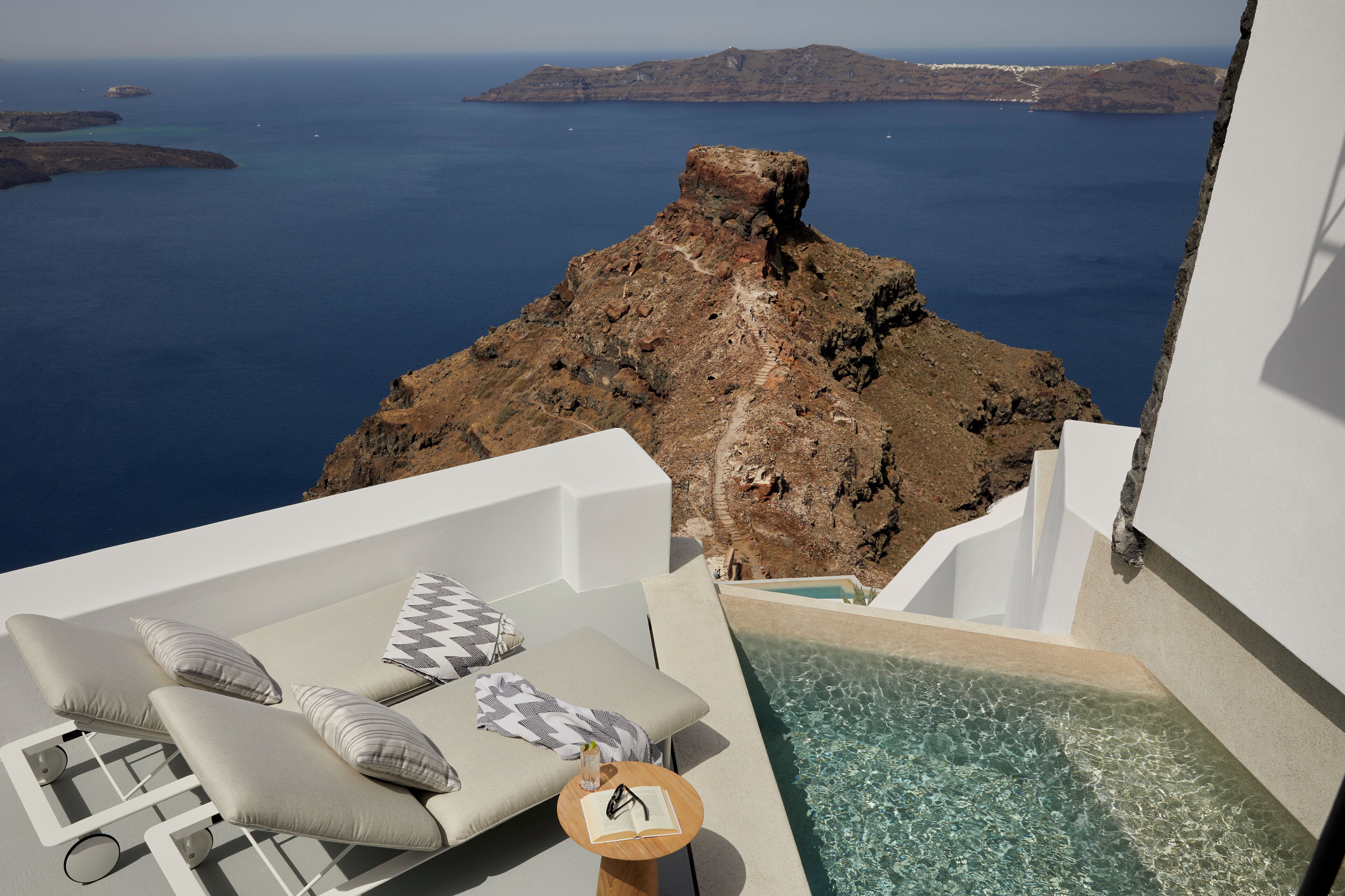 A sunlit outdoor lounge area with a view of the sea and a rocky island.