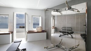 A modern room with a large mirror, exercise equipment, and a view of the sea through open doors.