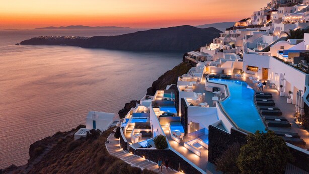 A resort with a pool, white buildings, and a view of the sea at sunset. - Grace Hotel, Auberge Collection (Santorini)