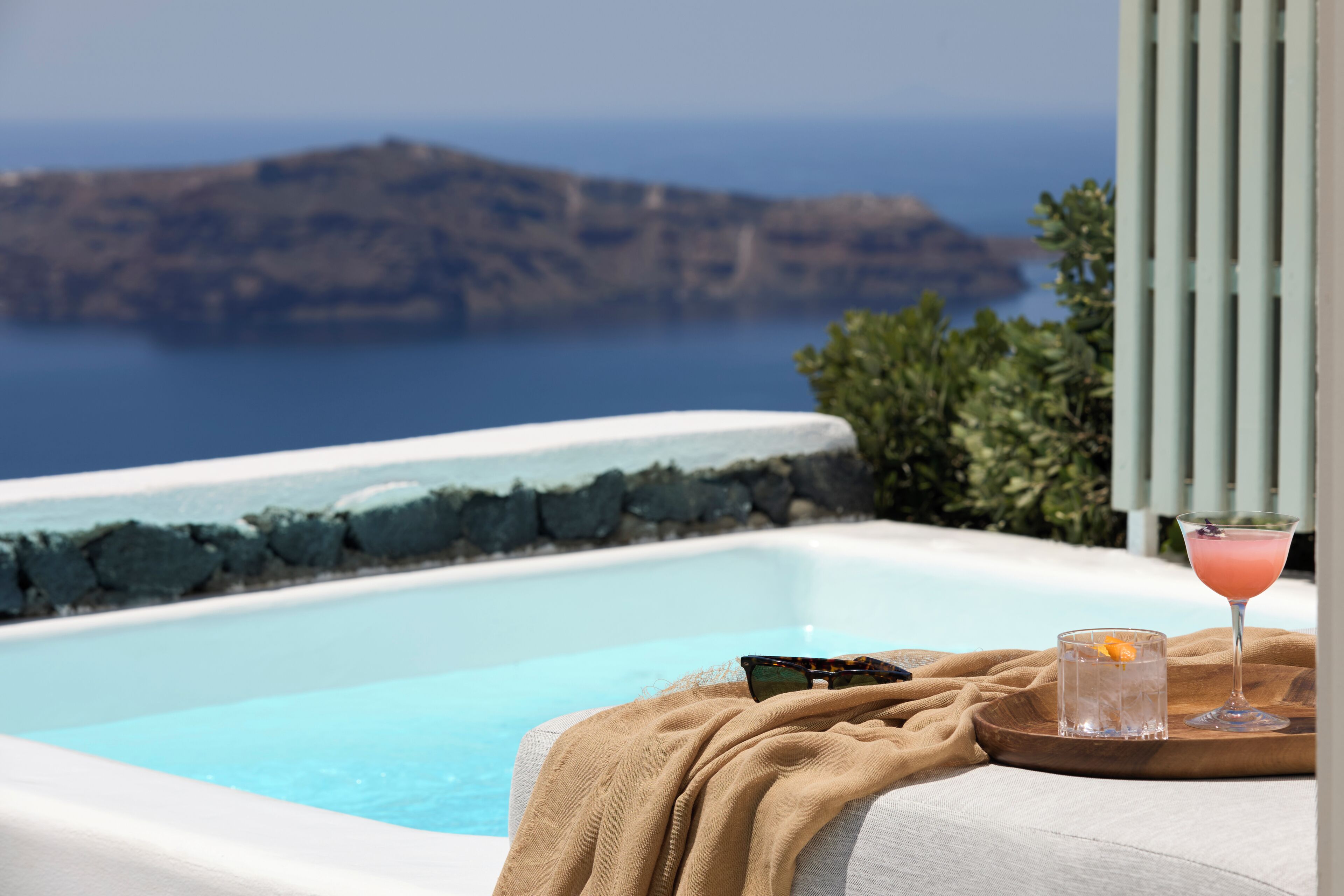 A pool with a view of a rocky island, a glass of drink, and a towel on a lounge chair.