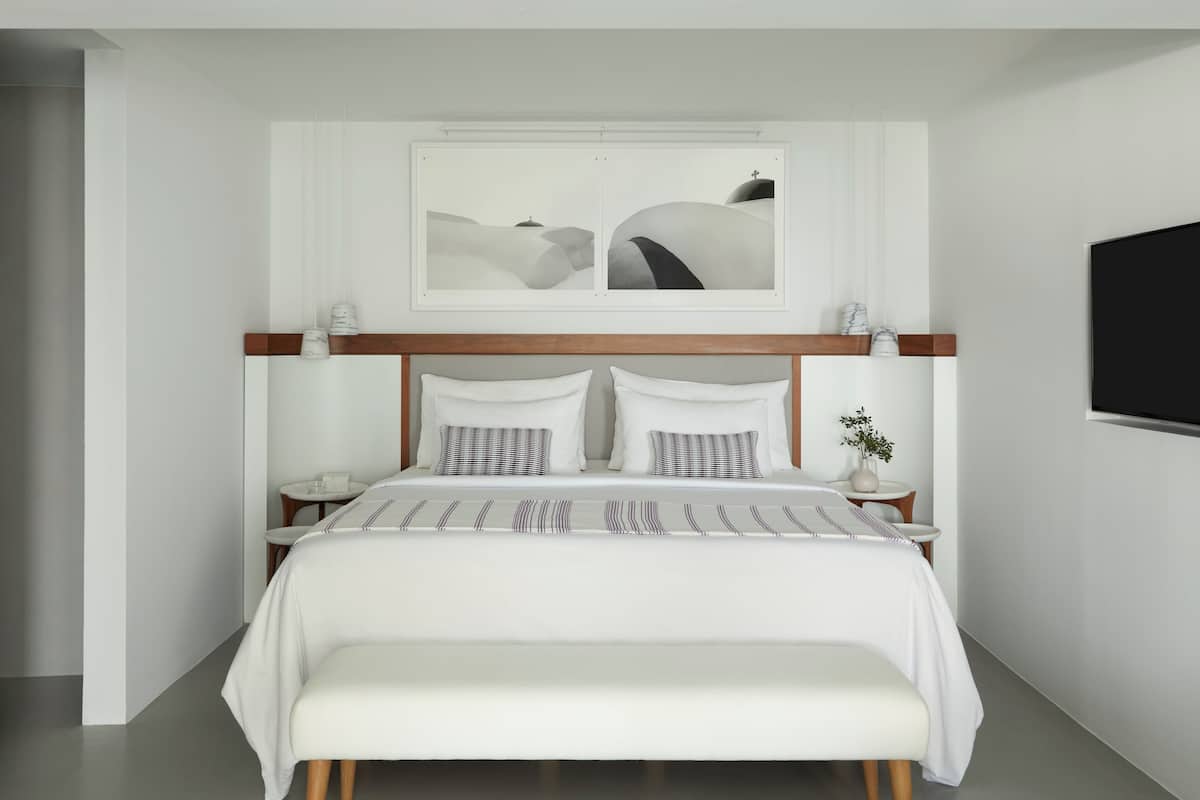 A modern bedroom with a large bed, bedside tables, a bench, and artwork on the wall.