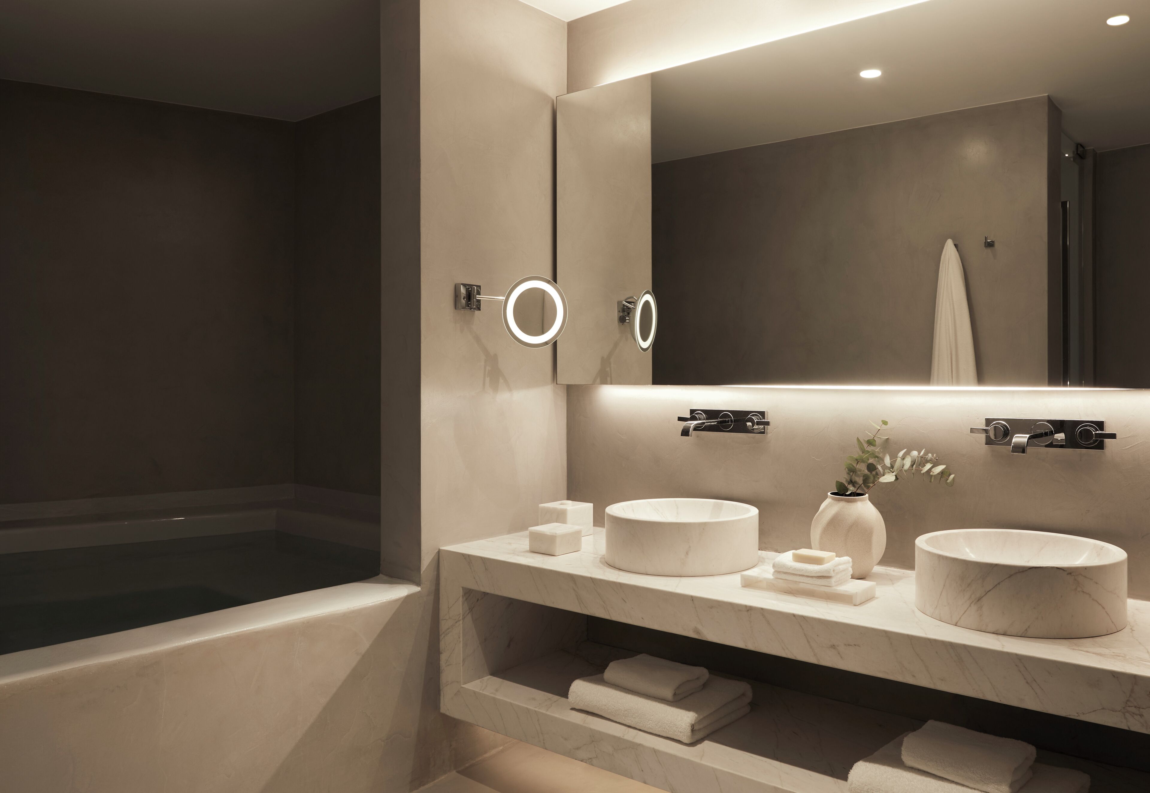 Une salle de bain moderne avec un grand miroir, deux petits miroirs ronds, une baignoire et un meuble-lavabo doté d’un lavabo rond et d’un plan de travail en marbre.
