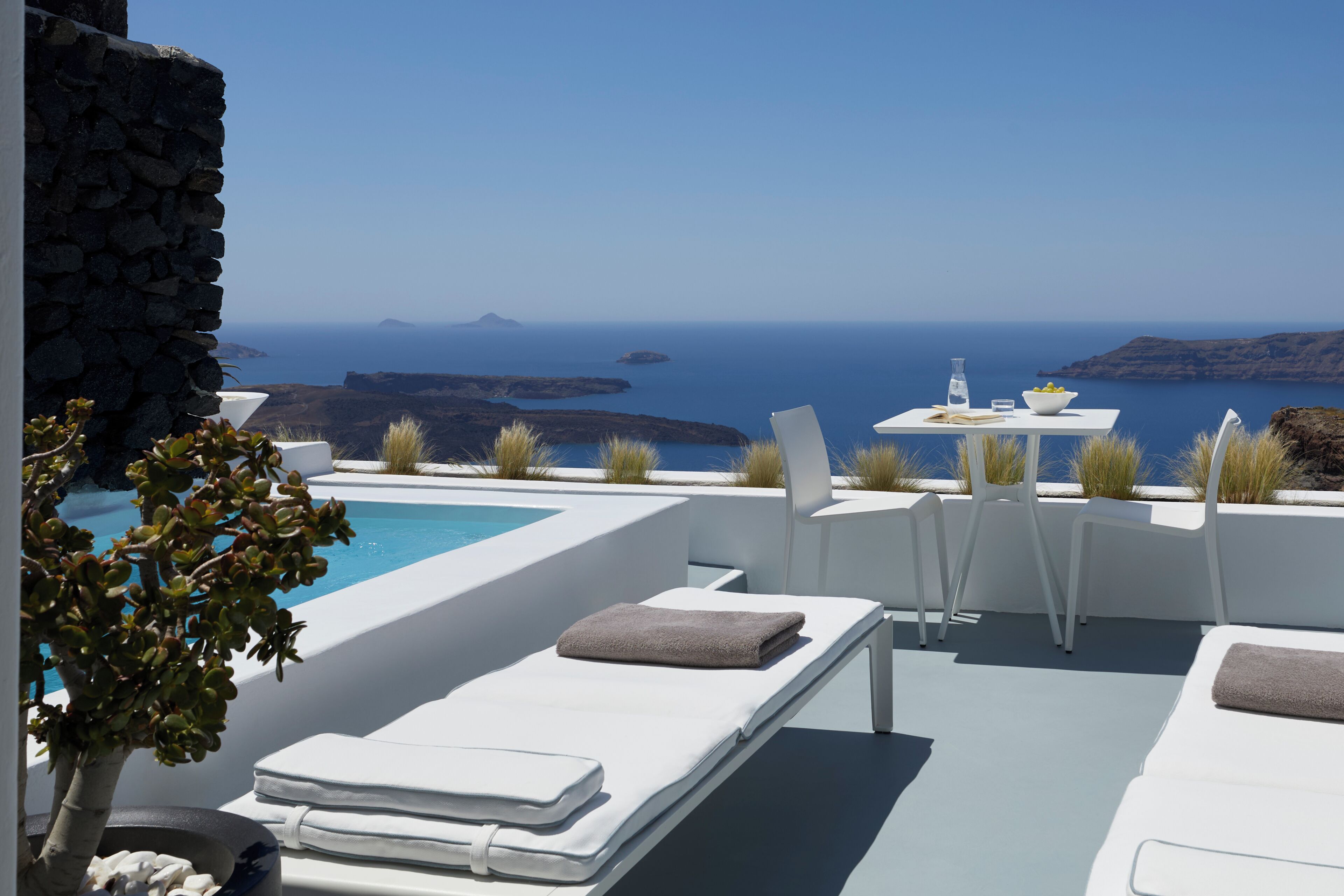 Uma área na piscina com espreguiçadeiras, uma mesa com uma cesta de frutas e vista para o mar e ilhas.