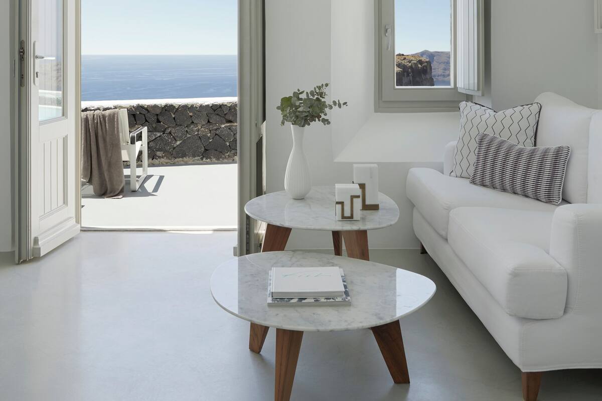 A modern living room with a white sofa, a round coffee table, and a view of the ocean through open doors.