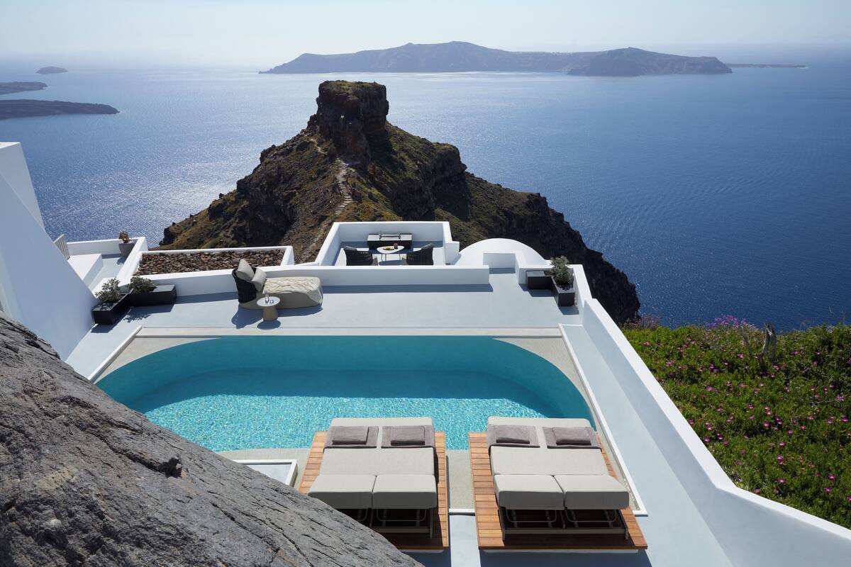 A pool with lounge chairs, a view of the sea, and a rocky landscape.