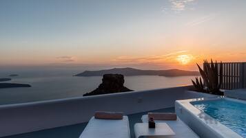 Et tag med swimmingpool, liggestole og havudsigt i solnedgang.