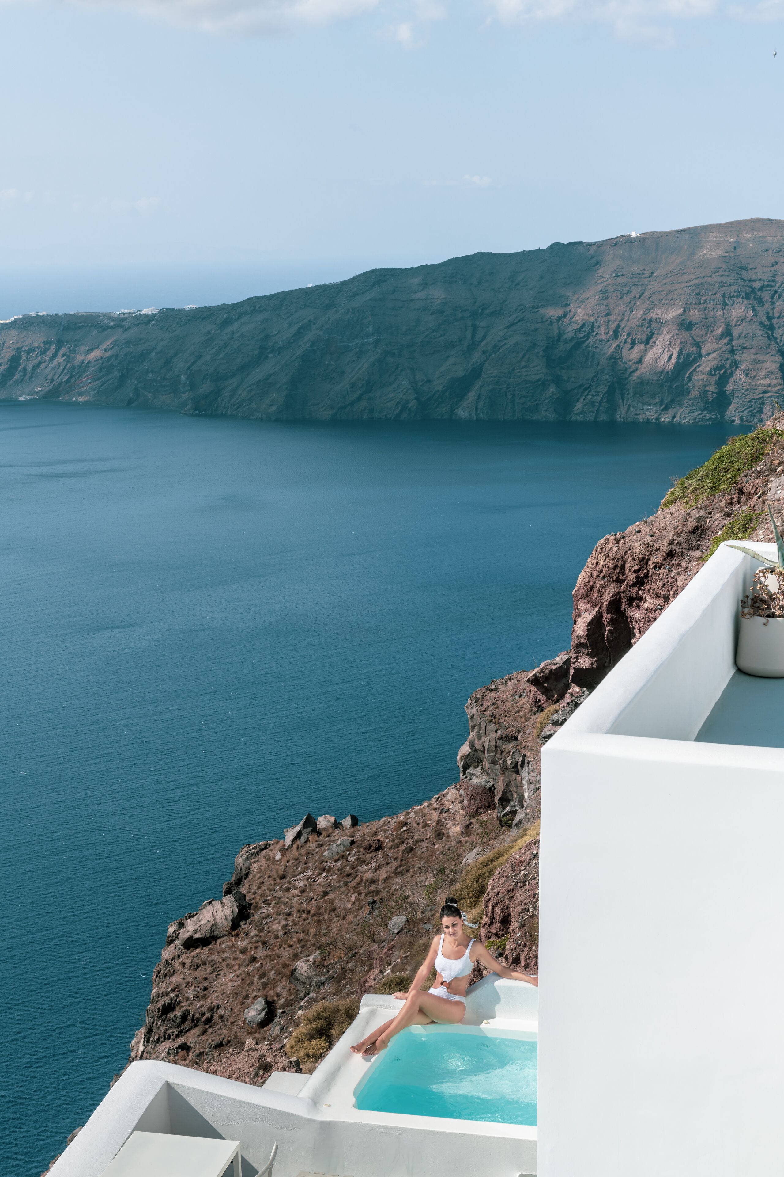 A person relaxing in a white infinity pool with a view of the sea and cliffs.