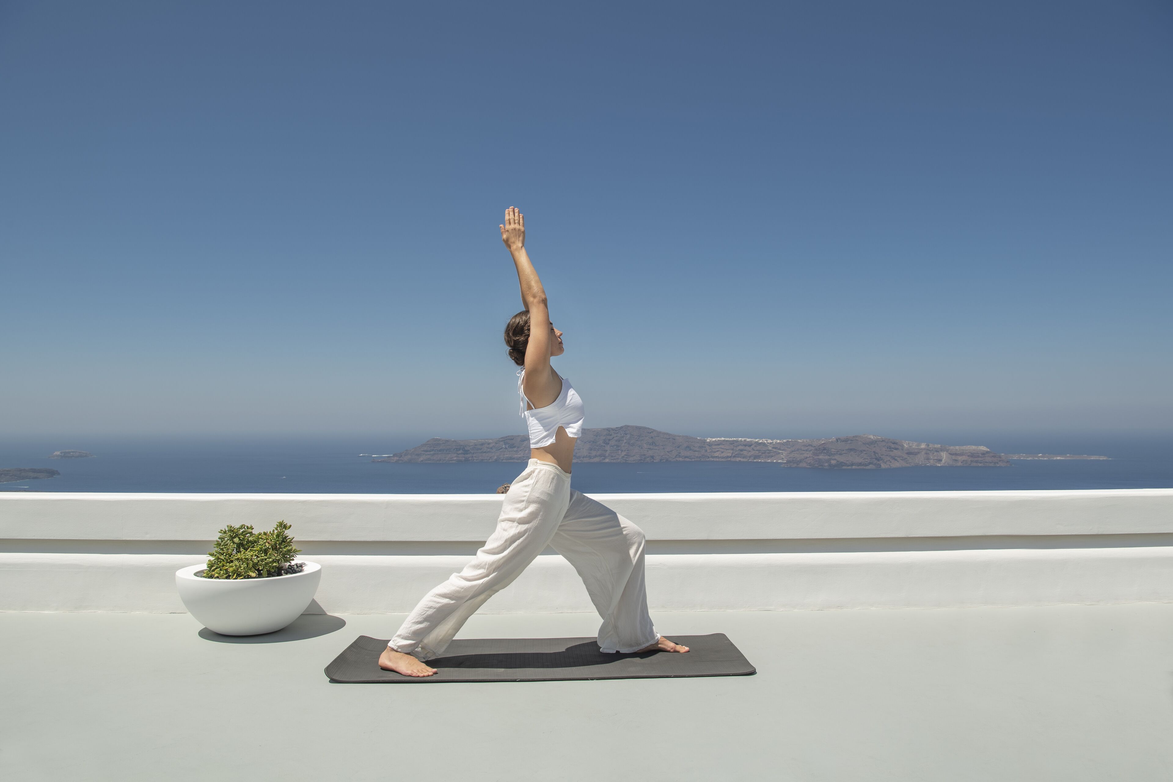 A person performing yoga on a rooftop with a view of the sea and distant islands.