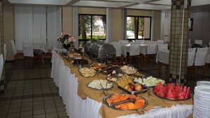 Montaje de bufé con diferentes alimentos, una parrilla y mesas dispuestas para comer.