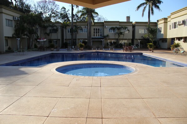 Una piscina con un jacuzzi circular en el centro, rodeado de sillones de descanso y palmeras.
