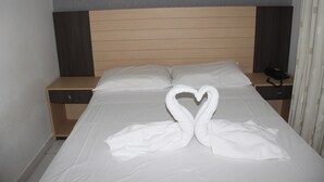Habitación de hotel con cama, cabecera de madera, mesita de noche y decoración de toalla con forma de corazón.