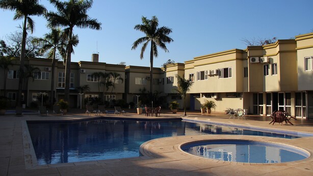 Un área de piscina con varias piscinas, palmeras y un edificio con unidades de aire acondicionado.