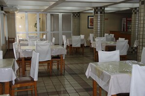 Un comedor con mesas cubiertas de plástico, sillas con fundas blancas y un piso de baldosas.