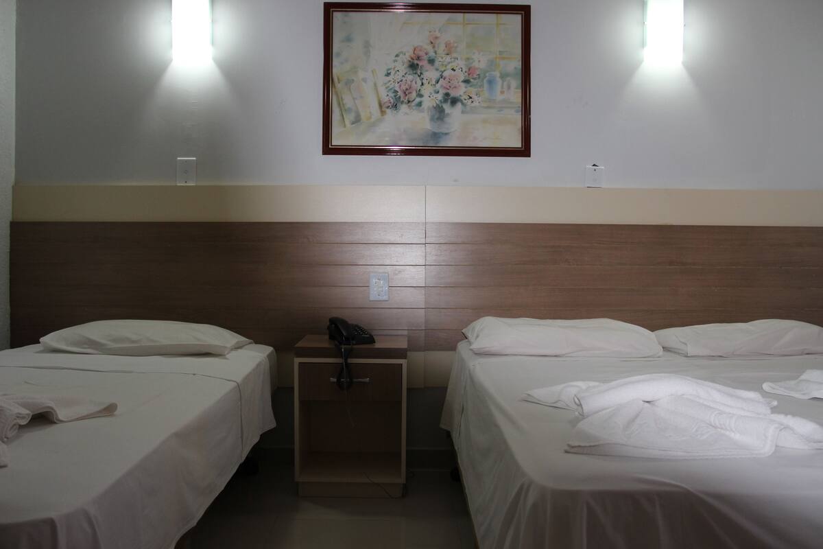 Una habitación de hotel con dos camas, una mesita de noche con teléfono y un cuadro en la pared.