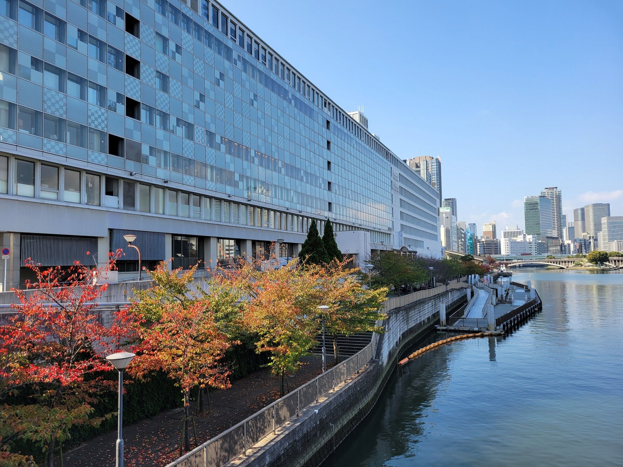 A modern building with a glass facade, a waterfront view, and a bridge connecting to another structure.