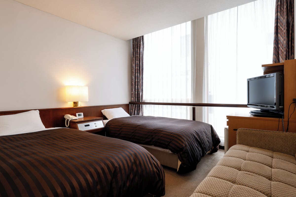 A hotel room with two beds, a television, a desk, and a lamp.