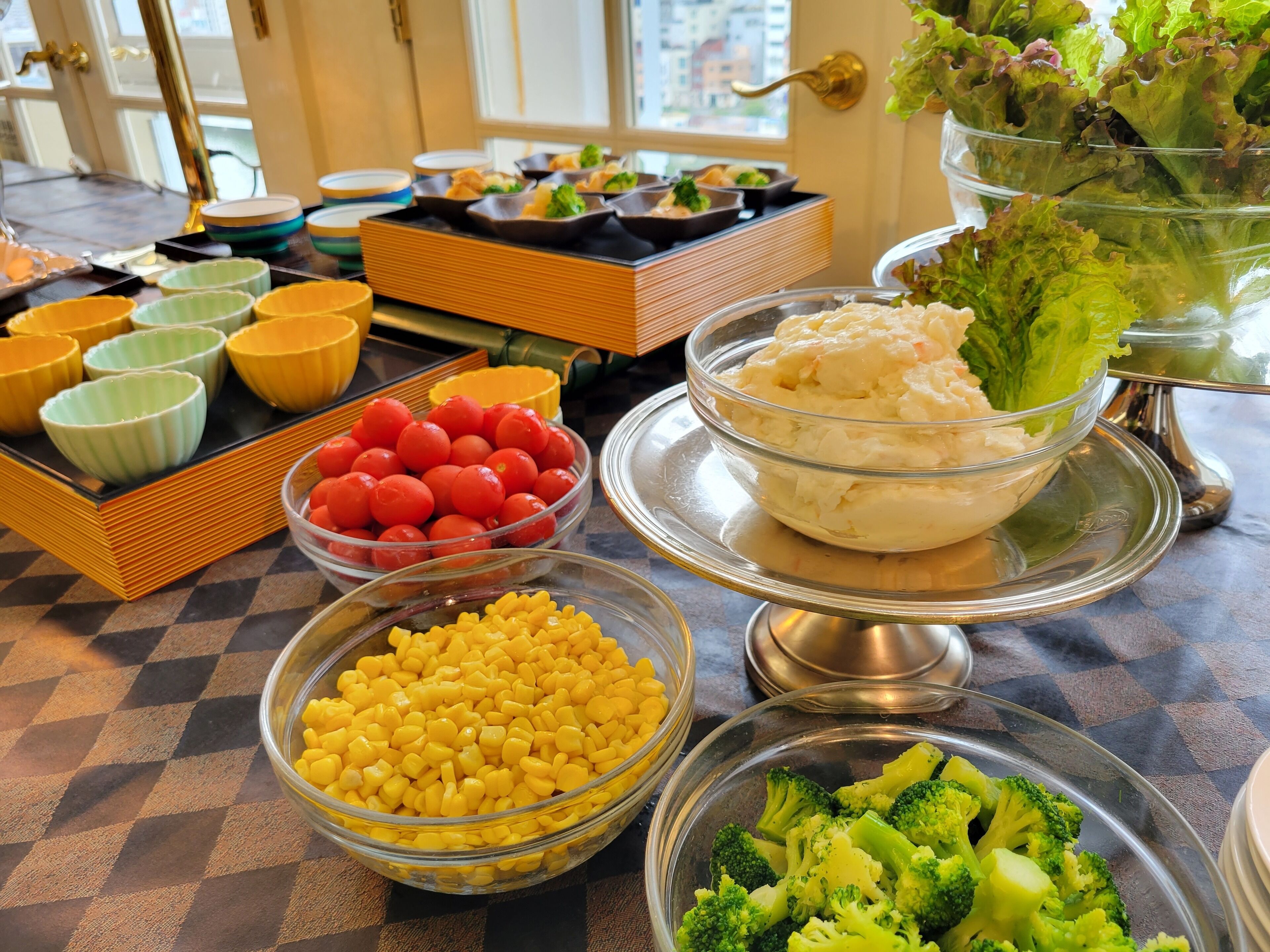 A buffet table with various food items including bowls of corn, tomatoes, and broccoli.