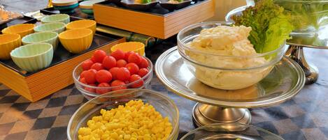 A buffet table with various food items including bowls of corn, tomatoes, and broccoli.