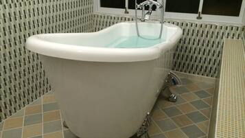 A white freestanding bathtub in a bathroom with patterned tiles and a window above it.