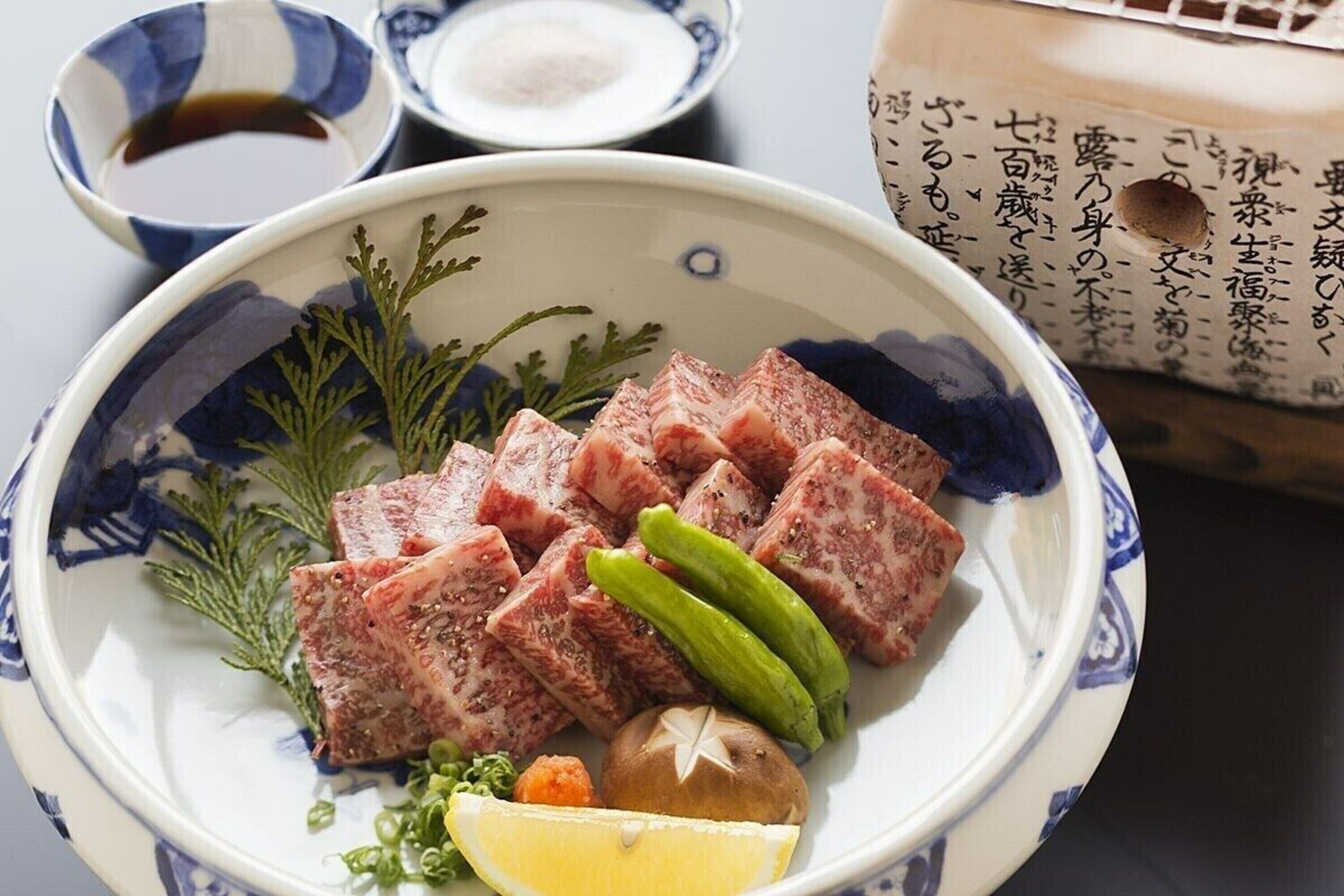 A plate of sliced meat with pickles and a lemon wedge.