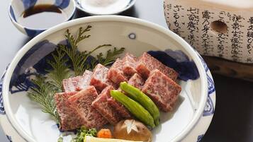 A plate of sliced meat with pickles and a lemon wedge.