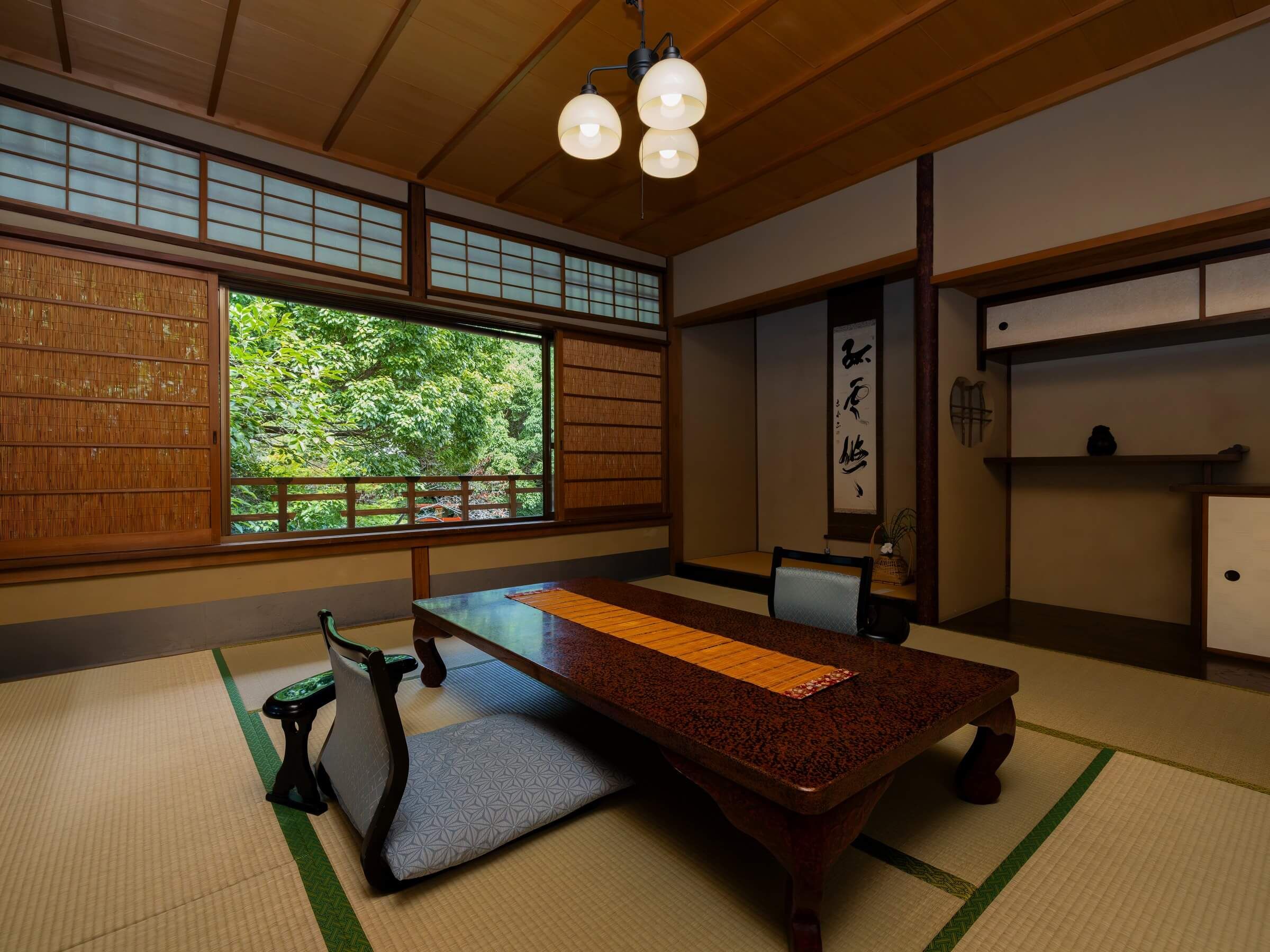 Een traditionele Japanse kamer met tatami vloerbedekking, een lage houten tafel, een groene stoel en uitzicht op groen door een groot raam.