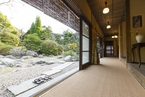 A traditional Japanese interior with tatami flooring, a view of a garden with rocks and trees, and a sliding door leading to another room. - Amami Onsen Nanten-en (Kawachinagano)