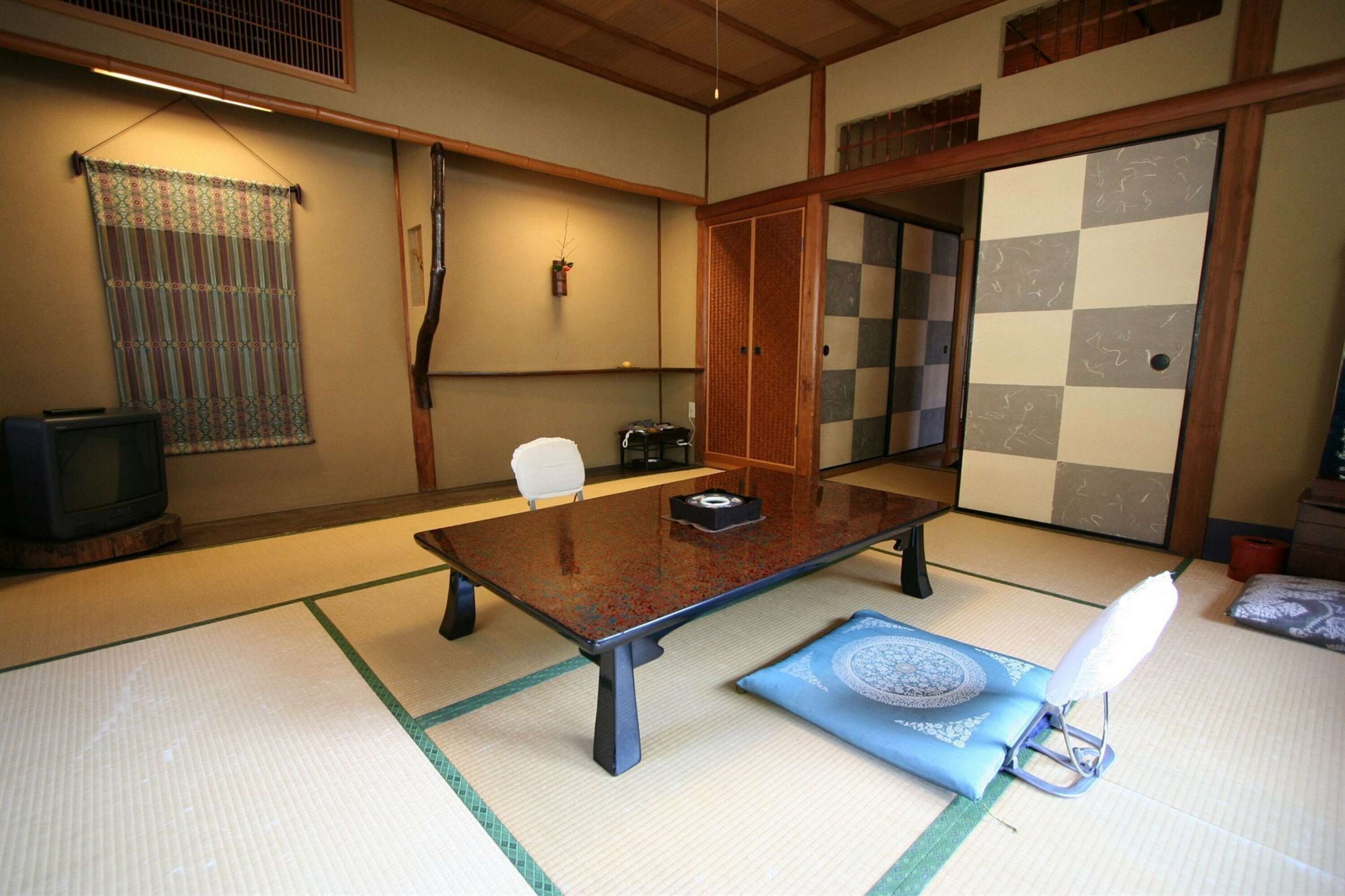 A traditional Japanese room with tatami flooring, a low table, two white chairs, a television, and a shoji screen.
