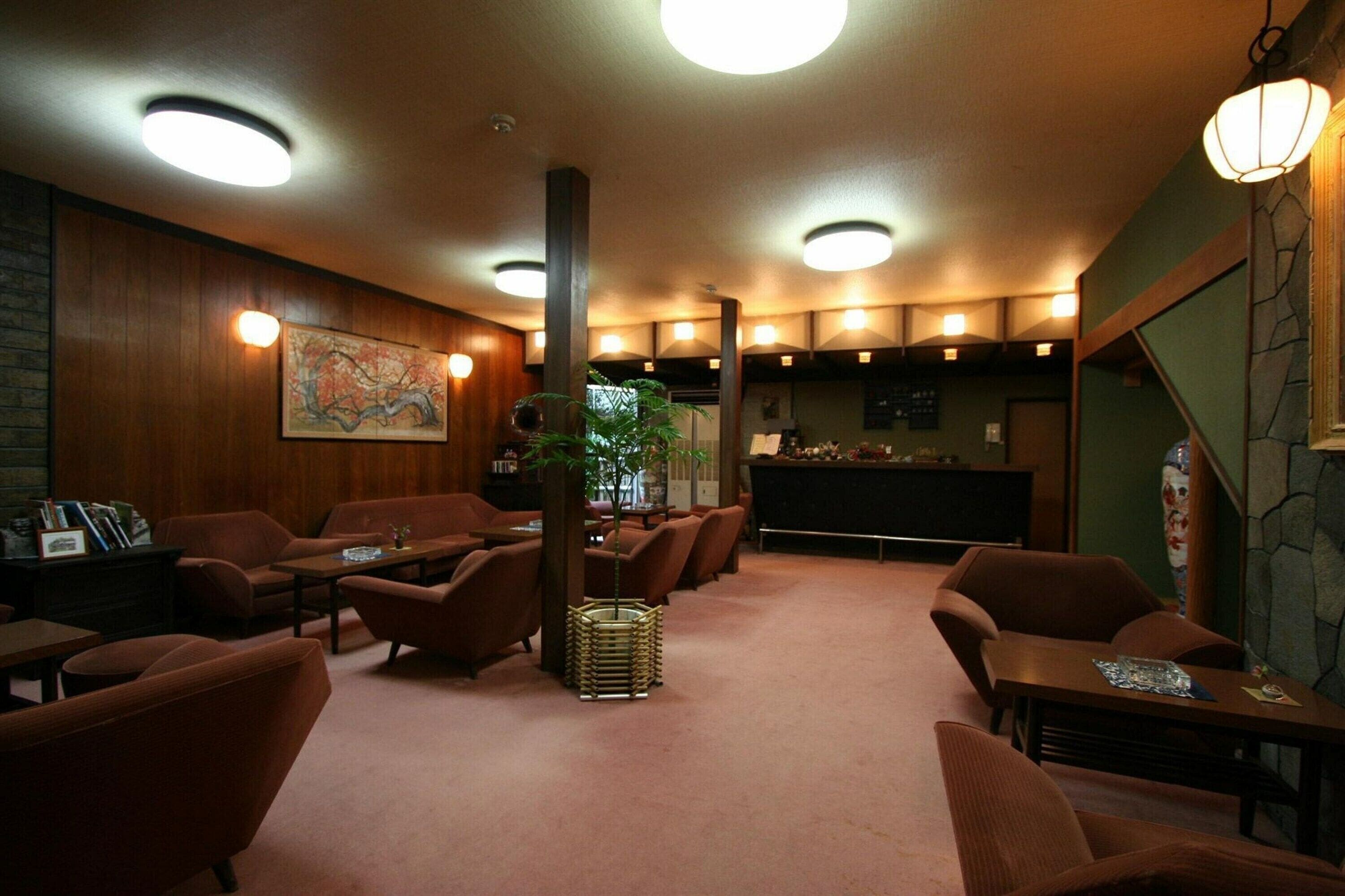 A cozy lounge area with wooden walls, a large painting, and a central plant. There are multiple seating options including sofas and chairs.