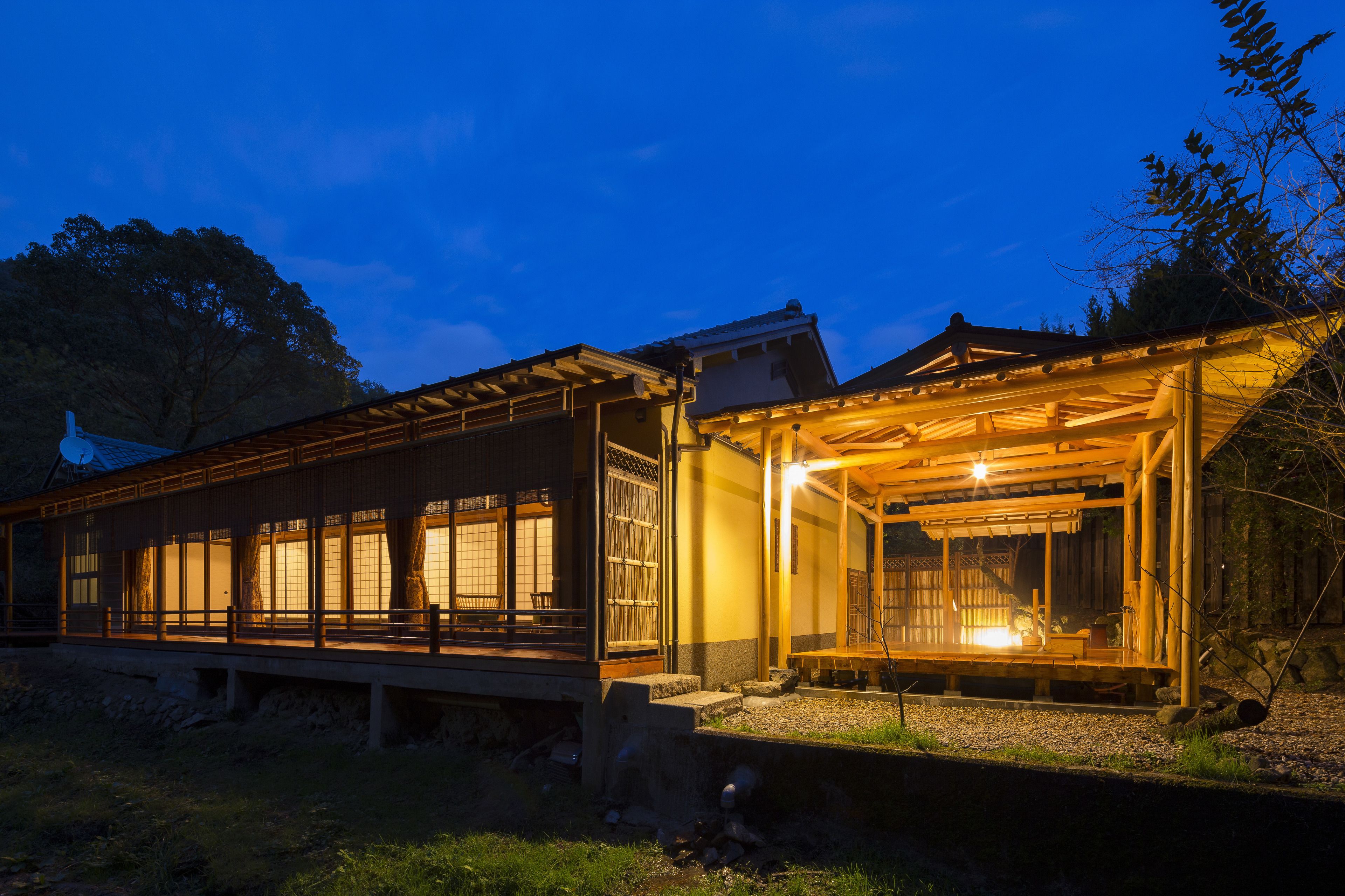Un edificio japonés tradicional con fachada de madera y ventanas amplias, que cuenta con un espacio de estar al aire libre cubierto.