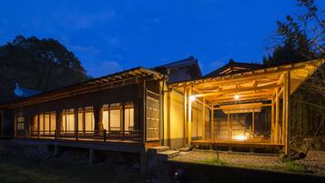 Un edificio japonés tradicional con fachada de madera y ventanas amplias, que cuenta con un espacio de estar al aire libre cubierto.