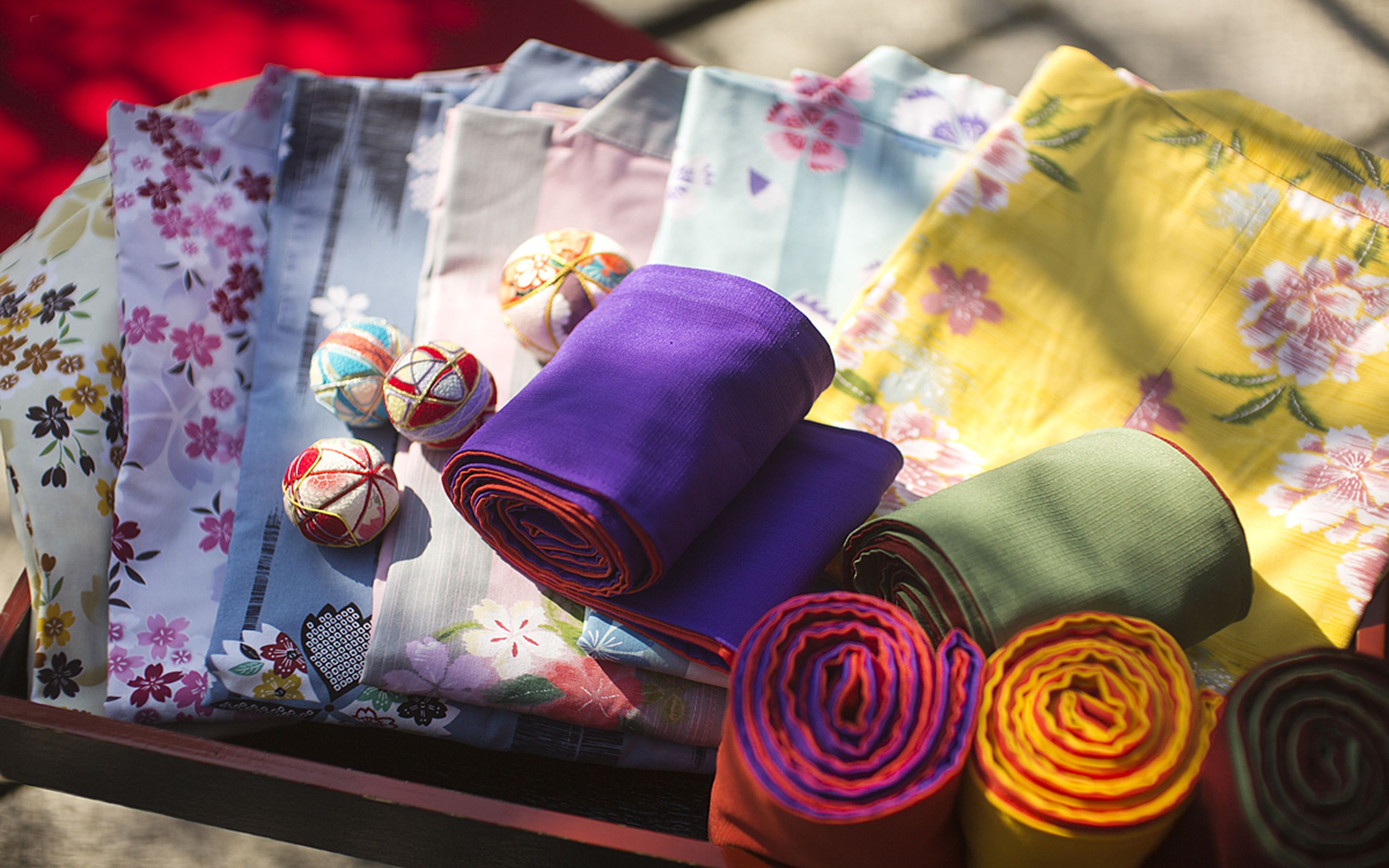 A tray with various fabrics and rolled textiles, including purple, yellow, and green materials, alongside colorful balls.