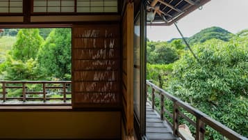 A traditional Japanese room with tatami flooring, a sliding door, and a balcony overlooking a lush garden.