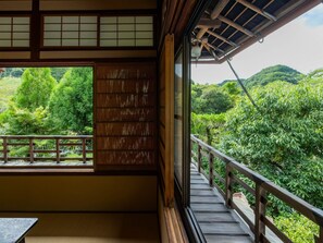 A traditional Japanese room with tatami flooring, a sliding door, and a balcony overlooking a lush garden. - Amami Onsen Nanten-en (Kawachinagano)