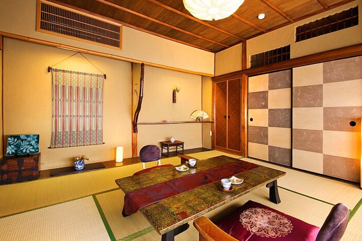 A traditional Japanese room with tatami flooring, a low table with cushions, sliding doors, and a hanging fan.