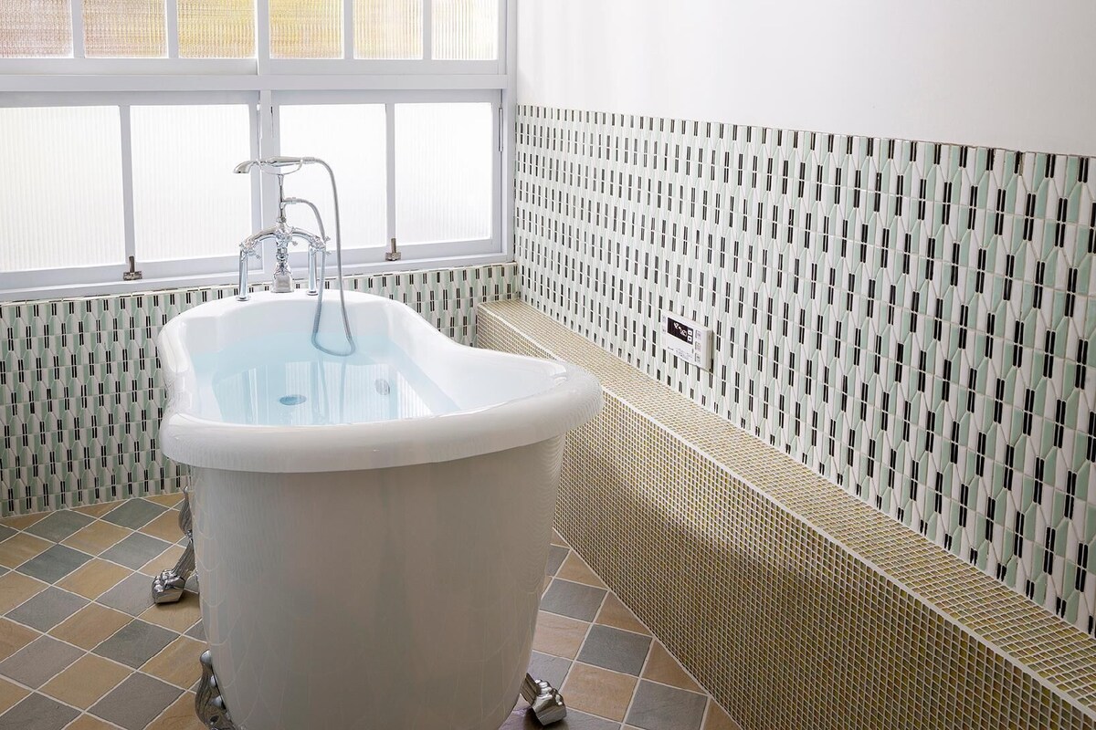 A bathroom with a freestanding bathtub, a window, and patterned walls.