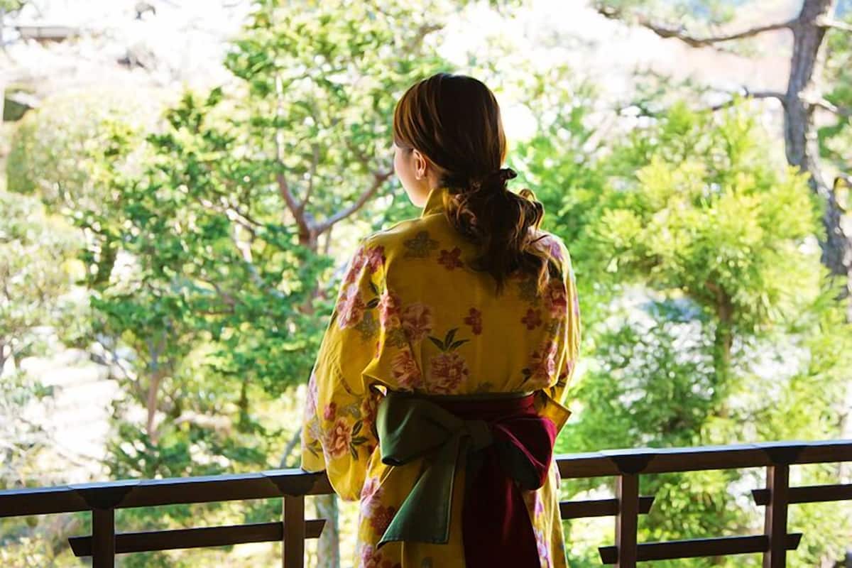 A person in traditional attire standing on a balcony with a view of trees.