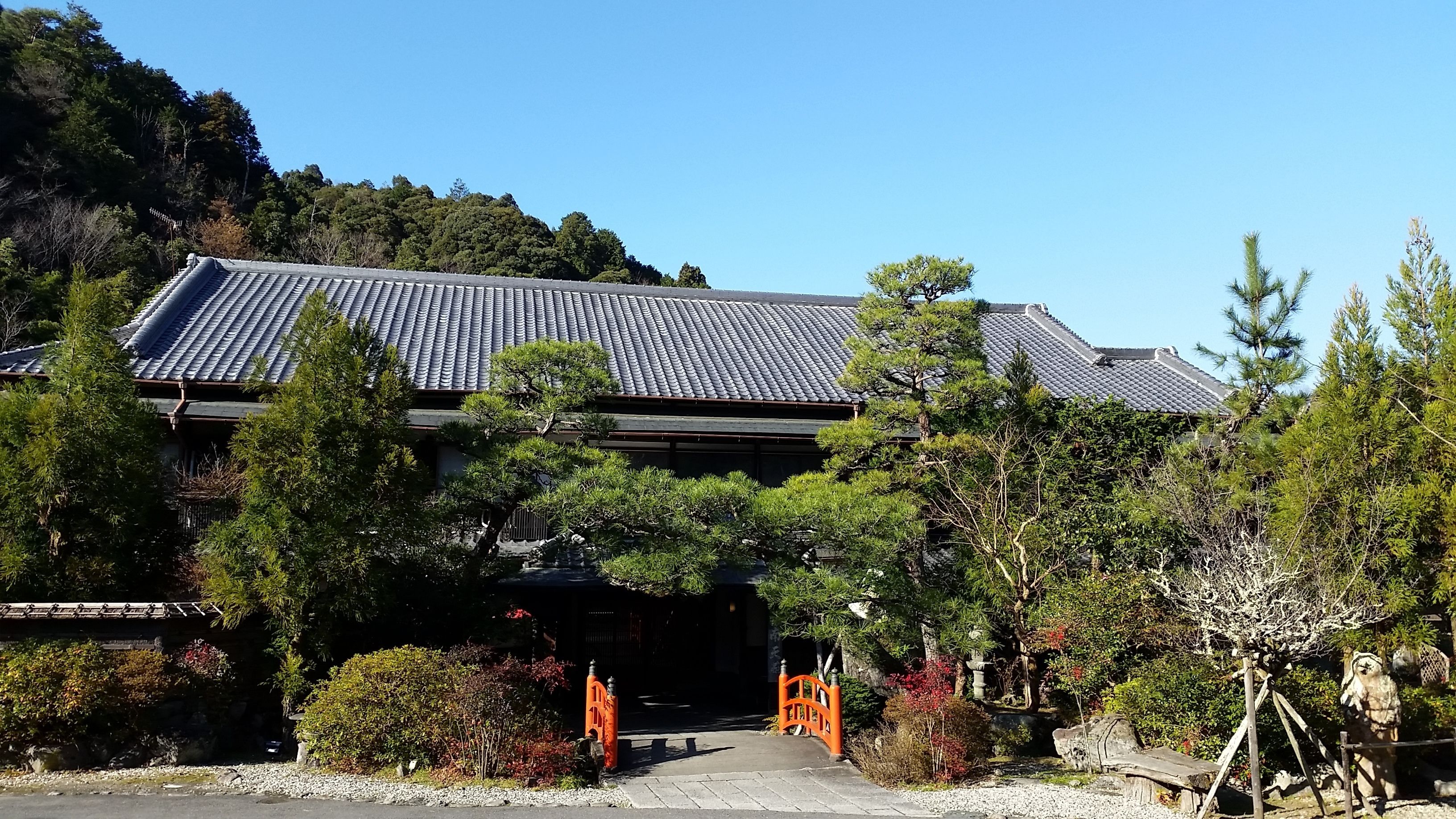 A traditional building with a tiled roof, surrounded by trees and shrubs.