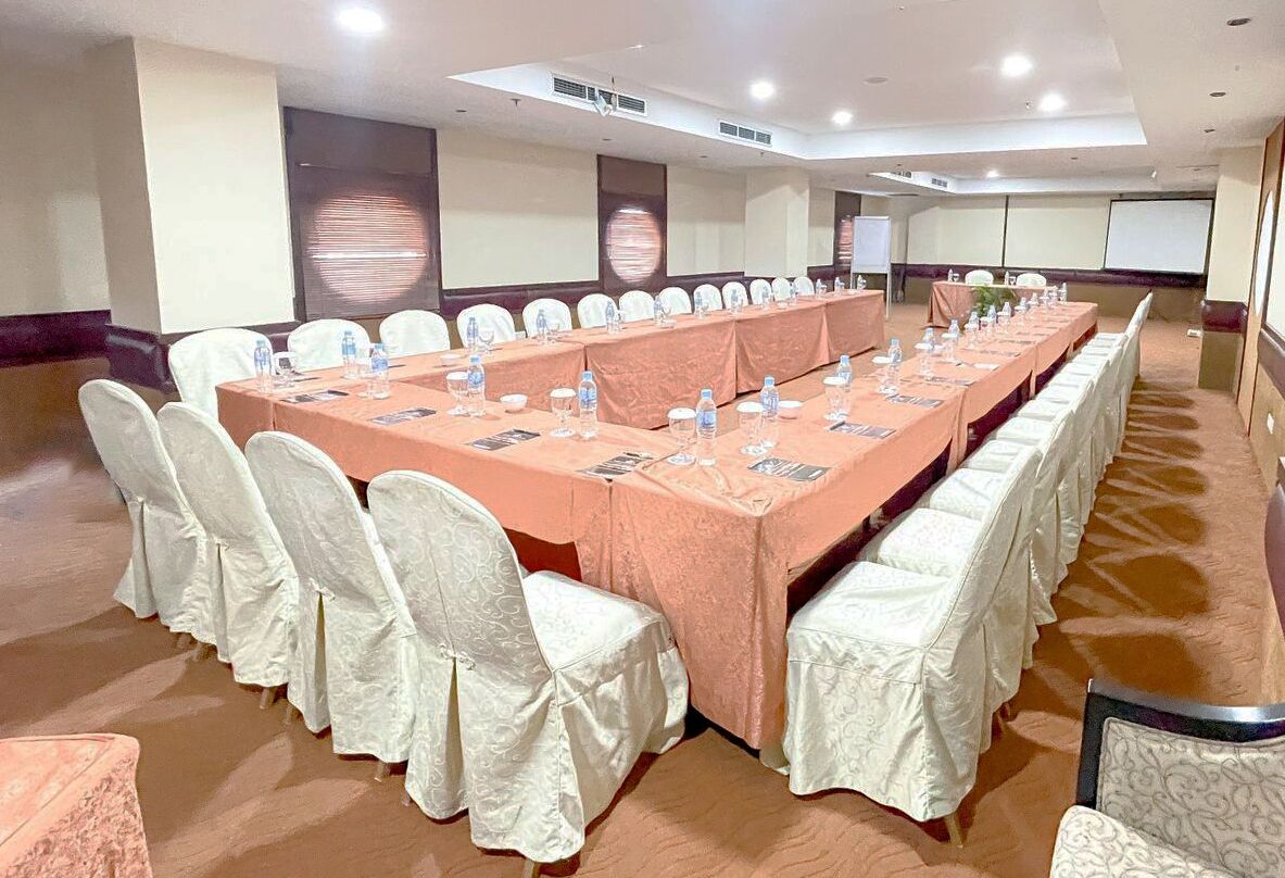 Uma sala de conferências com uma mesa comprida, cadeiras brancas e toalha de mesa cor de pêssego.