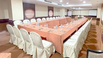 Uma sala de conferências com uma mesa comprida, cadeiras brancas e toalha de mesa cor de pêssego.