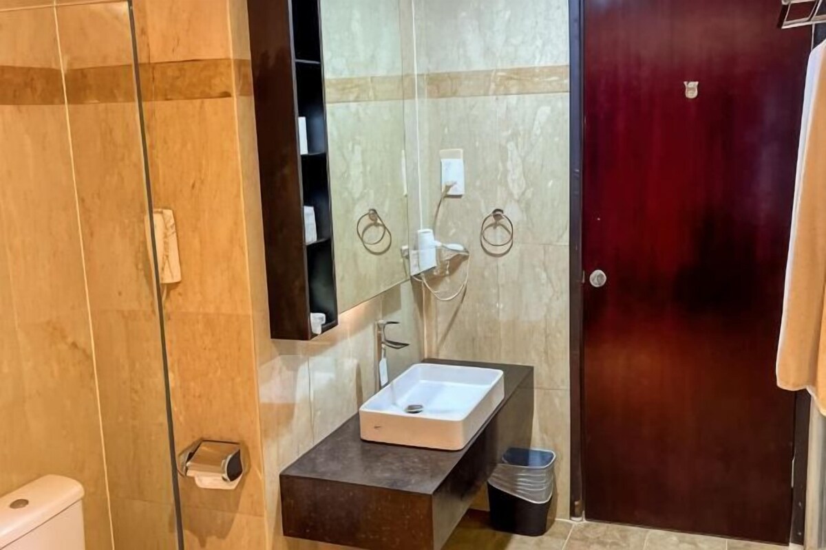 A bathroom with a glass shower enclosure, a white sink, a dark countertop, and a wooden door.