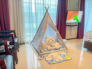 A cozy living room with a teepee play tent, plush toys, and a TV on a stand. - Pacific Palace Hotel (Batam)